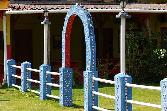 Example of a little blue fence around a beach home decorated with a variety of white and colored shells