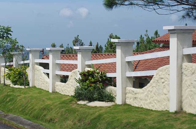 Photo Example of a fence made of beige curved wall segments, white cement columns and white painted wood bars