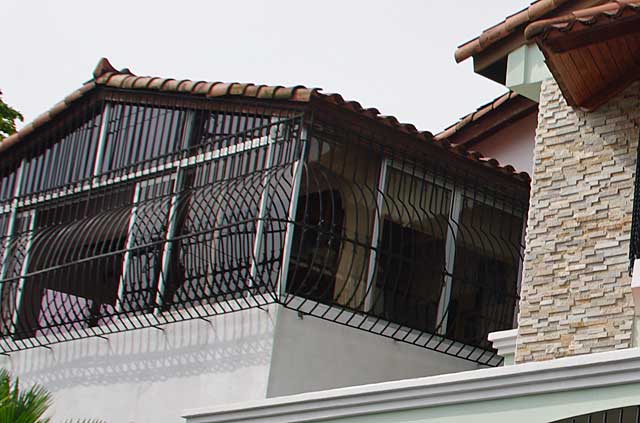 Photograph of some simple but decorative metal security bars covering the windows of the upper floor of this house