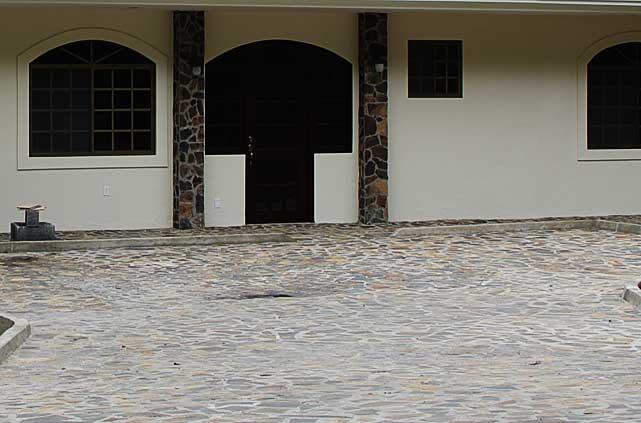 Photo example of a driveway and some columns covered with dark colored stone plates. That combine well together with the beige walls and dark brown windows