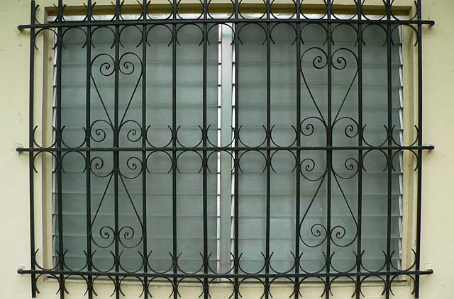 Photo example of an old jalousie type window with decorative black painted security metal bars
